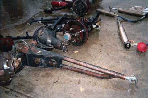 1990 Ford Bronco - front differential axle, a long radius arm, brake hub and shock absorbers are laid out on a stained garage floor.