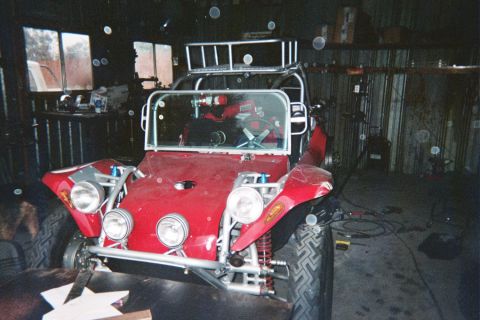 1990 Ford Bronco - red fiberglass dune buggy with a tubular roll cage and round headlights sits under construction inside a dim garage.