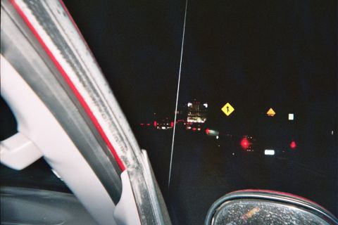 1990 Ford Bronco - Night view through a windshield of distant taillights and yellow diamond warning signs along a dark road.