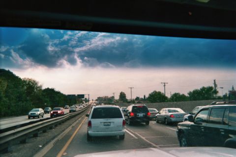 1990 Ford Bronco - View through a windshield of bumper-to-bumper freeway traffic with vans and cars under dark dramatic storm clouds.