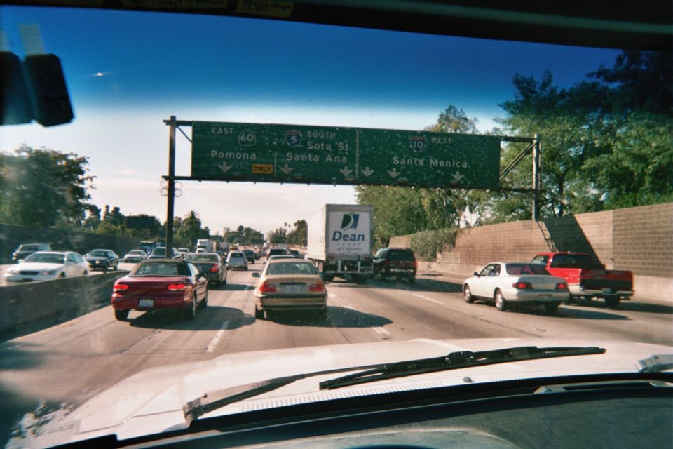 Freeway traffic seen through a windshield with green overhead exit signs for Pomona, Santa Ana and Santa Monica