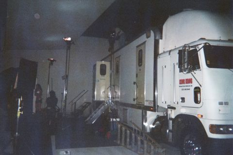 1990 Ford Bronco - white semi-truck cab and white production trailers parked indoors under film lighting stands in a dim soundstage.