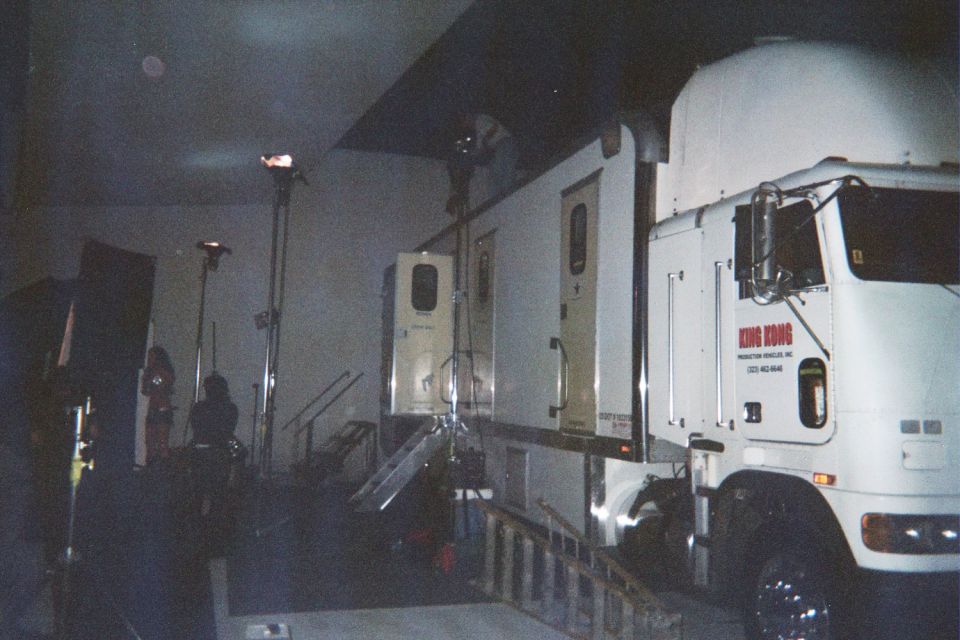 Dimly lit interior with a white semi truck cab and production trailers under stage lighting stands