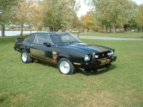 1978 Ford Mustang II - A black 1970s coupe with distinctive cobra graphics is shown from a three-quarter front angle on-road view.