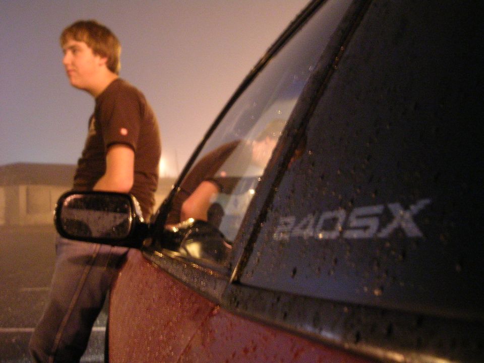 Guy leaning on a red car with "240SX" on the door in the rain