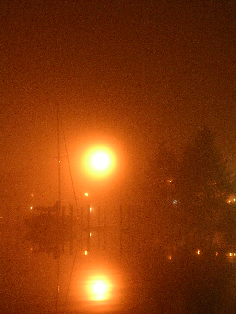 Boat docked at a pier with bright lights reflecting on the water at night