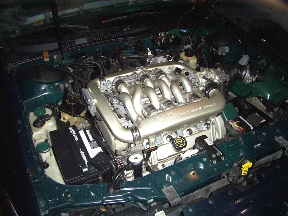 Green engine bay with a V6 24 valve DOHC engine, battery, and hoses. The engine has silver intake manifolds