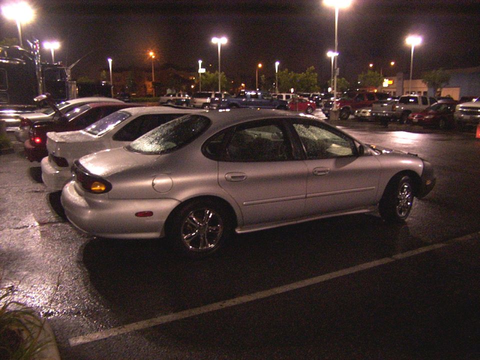 Silver sedan parked in a wet lot at night, other cars visible