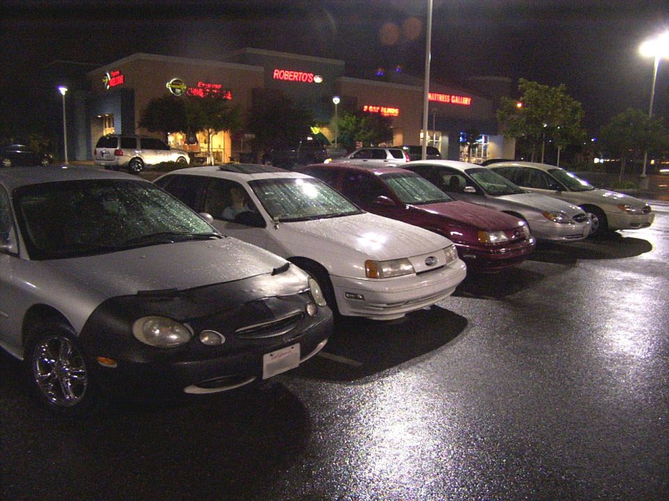 Silver Ford Taurus with car bra, parked in a lot at night