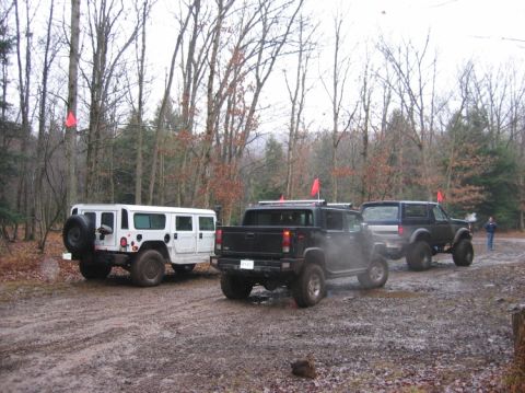 1995 Ford Bronco - A white Hummer, a black pickup truck, and a dark SUV are parked on a muddy road in a forest with red flags on trees.
