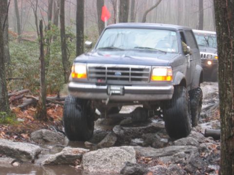 1995 Ford Bronco - A modified Ford Bronco tackles a challenging off-road course with another vehicle following closely.