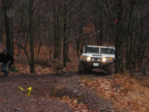 1995 Ford Bronco - A white SUV is being pulled by a winch cable through a muddy, wooded area.