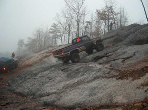 1995 Ford Bronco - Two trucks navigate a foggy, rocky terrain during an off-road excursion.