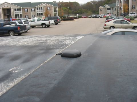 1988 Ford Bronco - A car stereo antenna is visible on a dark surface, with a parking lot and apartment buildings in the background.