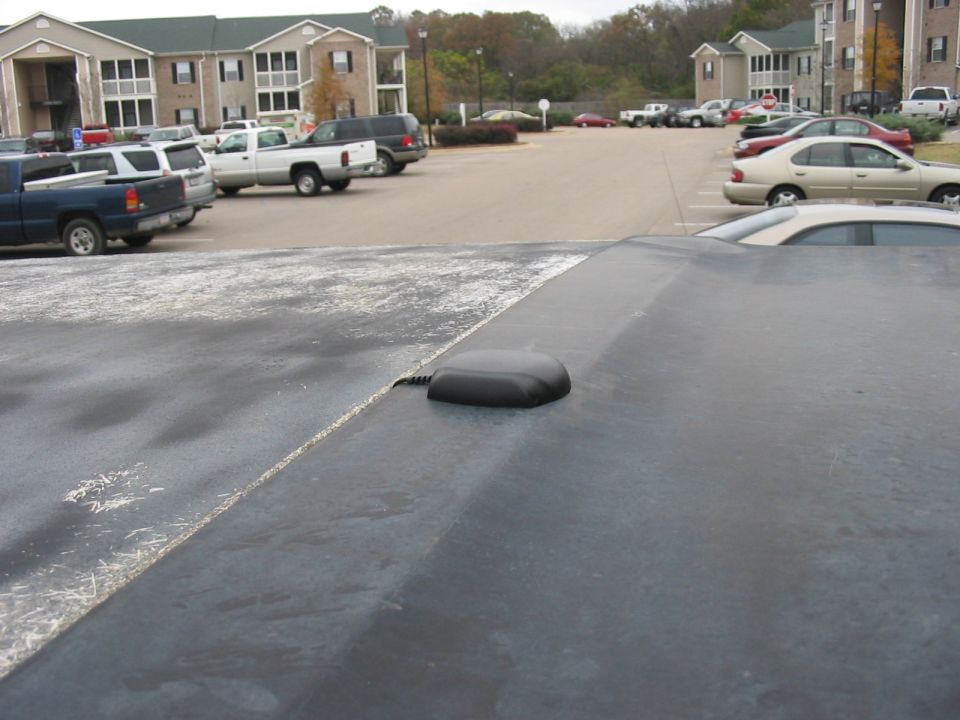 Car stereo antenna on a dark surface with a parking lot in the background