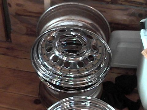 1995 Ford Bronco - Several chrome wheels are stacked on a wooden floor, with a white storage bin in the background.