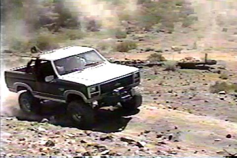 1984 Ford Bronco - This Ford Bronco is kicking up dust as it navigates a rough, outdoor landscape.