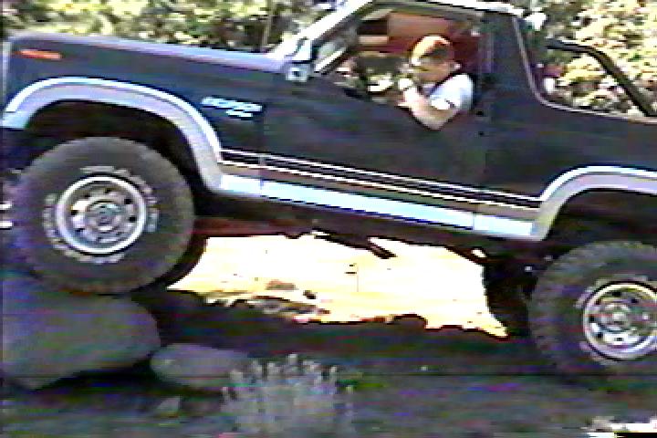 Dark blue topless lifted Bronco crawling over rocks at a water crossing