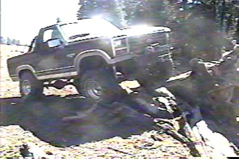 1984 Ford Bronco - Ford Bronco navigating rough terrain, climbing over logs.