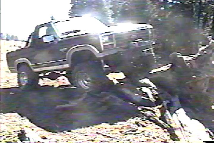 1980s Ford Bronco climbing over logs and dirt