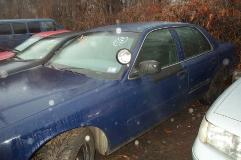 1991 Ford LTD Crown Victoria - A blue sedan, possibly a police car due to the spotlight, is seen in a lot with other vehicles.