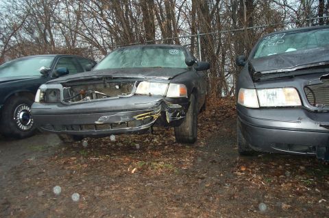 1991 Ford LTD Crown Victoria - Two damaged vehicles sit in an outdoor lot, with one showing significant front-end damage.