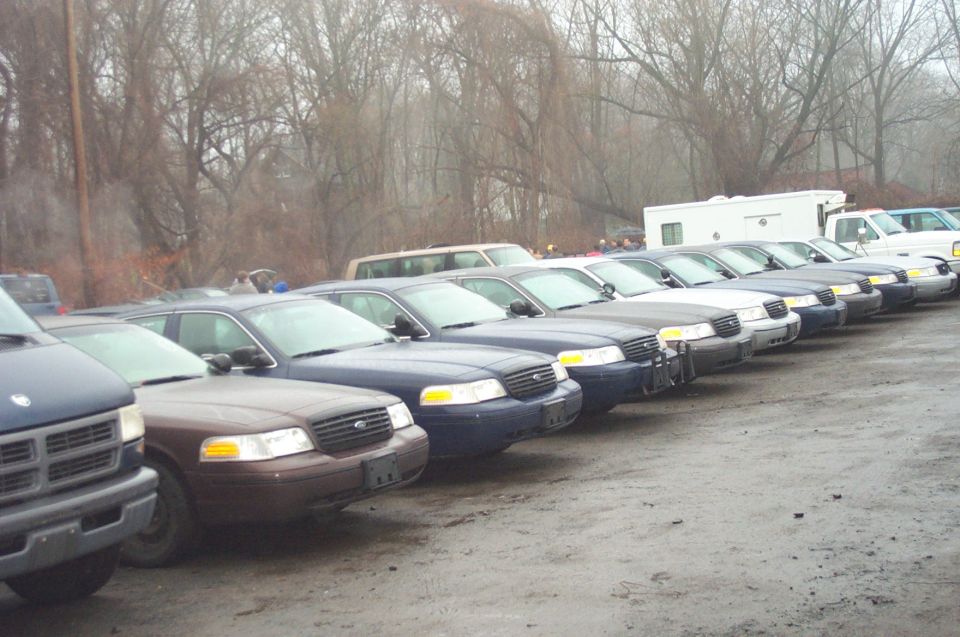 Several Ford Crown Victoria police cars parked in a lot, some dark blue, one brown