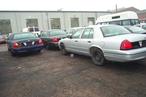 1991 Ford LTD Crown Victoria - Several Ford Crown Victoria sedans are parked outdoors in a gravel lot near a building.
