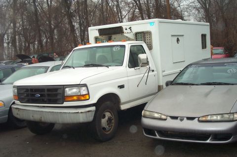 1991 Ford LTD Crown Victoria - A white Ford F-series truck with a box body is parked in an outdoor lot next to other vehicles.