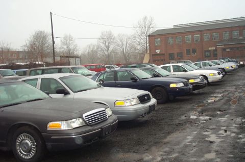 1991 Ford LTD Crown Victoria - A row of Ford Crown Victoria police cars are parked outside a brick building on a cloudy day.
