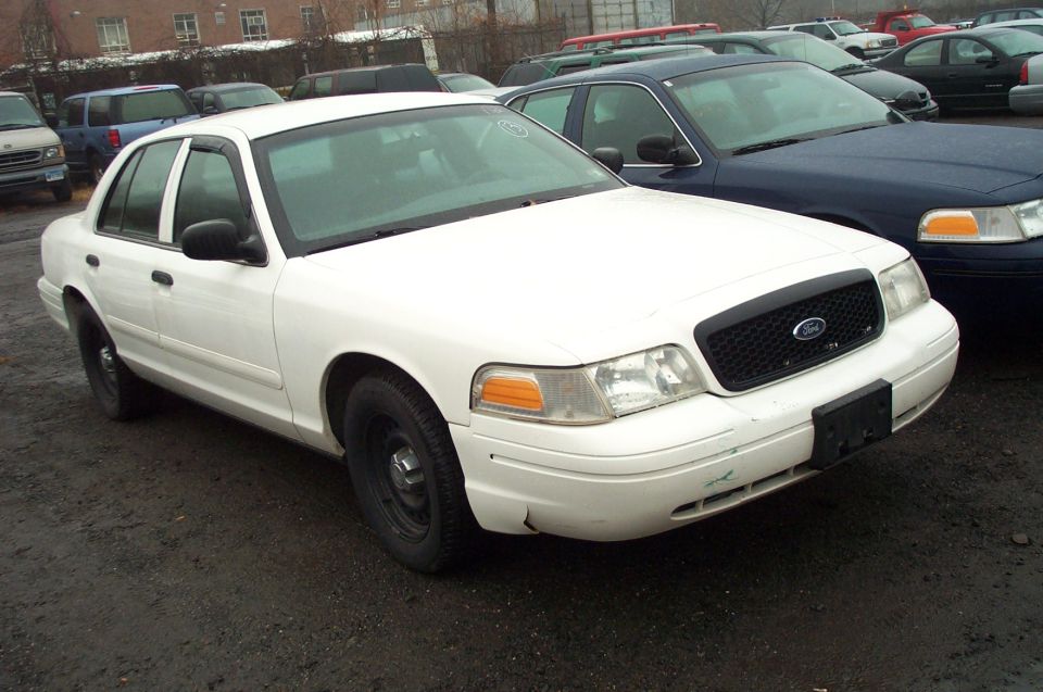 White Ford Crown Victoria parked outside, front end visible. Another dark blue car is next to it