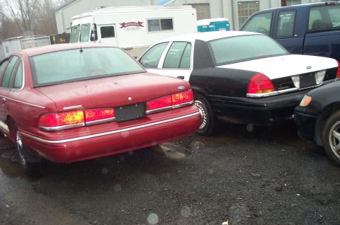 1991 Ford LTD Crown Victoria - Two Ford Crown Victorias, one a police car, are parked outdoors on a wet surface.