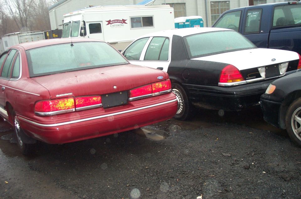 Rear view of a black and white Ford Crown Victoria police car parked next to a red Ford Crown Victoria