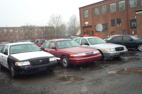 1991 Ford LTD Crown Victoria - Several Ford Crown Victorias are parked in a lot on a cloudy day, with brick buildings in the background.