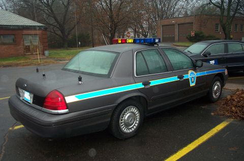 1991 Ford LTD Crown Victoria - A police car with a light bar and side decals is parked on a wet asphalt lot next to another vehicle.
