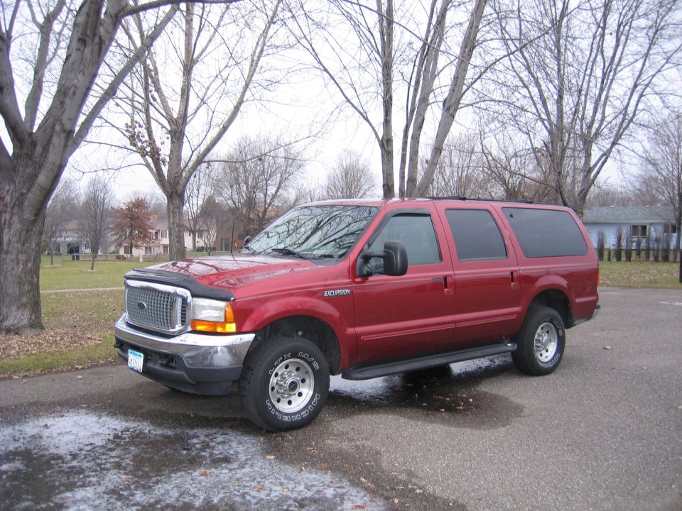Dark red Ford Excursion SUV parked outdoors, front three-quarter view, bare trees behind