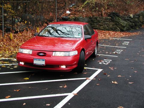 1992 Ford Taurus - A red 1992 Ford Taurus is parked in a lot, with autumn leaves scattered on the ground.