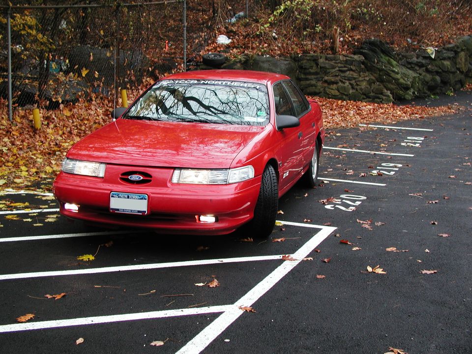 Red 1992 Ford Taurus parked in a lot with fallen leaves