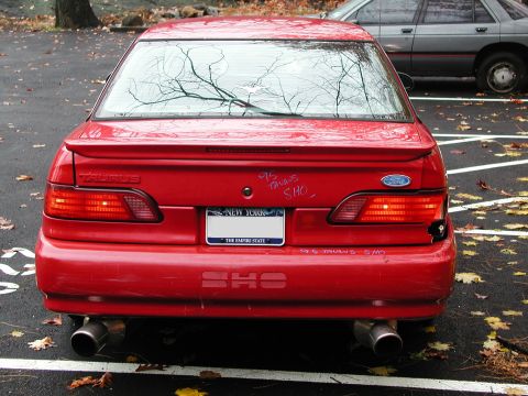 1992 Ford Taurus - A red 1995 Ford Taurus SHO is seen from the rear, parked in a lot with another vehicle visible.