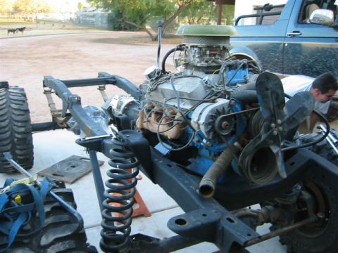 1994 Ford Bronco - The engine and chassis are being worked on, with a blue SUV visible in the background.