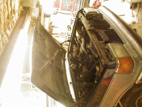 1987 Ford Bronco - The engine compartment of a vehicle is exposed with the hood raised, revealing the mechanical parts within.