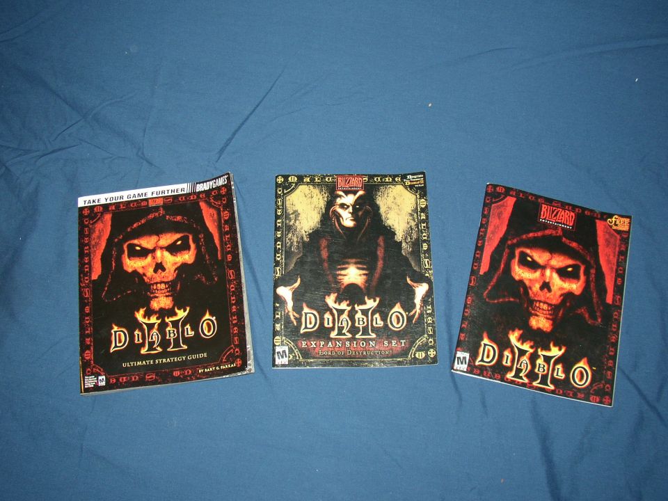 Three Diablo game boxes, including an ultimate strategy guide and an expansion set, laid out on a blue surface