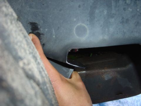 1998 Ford Taurus - Close-up view of a vehicle's underside, showing a gap and a hand reaching into it.