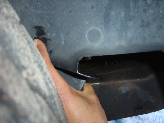 Hand reaching into a gap in the vehicle's undercarriage, revealing a dark interior