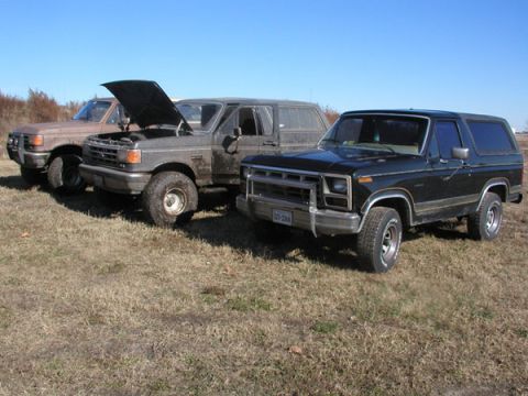 1988 Ford Bronco - Three Ford Broncos are parked in a dry, grassy field under a clear blue sky.