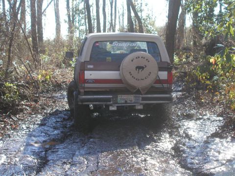 1988 Ford Bronco - This 1988 Ford Bronco navigates a challenging muddy path surrounded by trees.