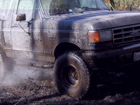 1988 Ford Bronco - This Ford Bronco is navigating through a muddy terrain, with water and dirt splashing around its tires.