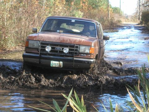 1988 Ford Bronco - This brown 1987 Ford F-150 navigates a muddy trail, kicking up water and dirt.