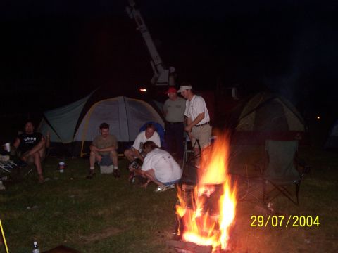1979 Ford F-150 - A group of people are gathered around a campfire at night, with tents set up in the background.