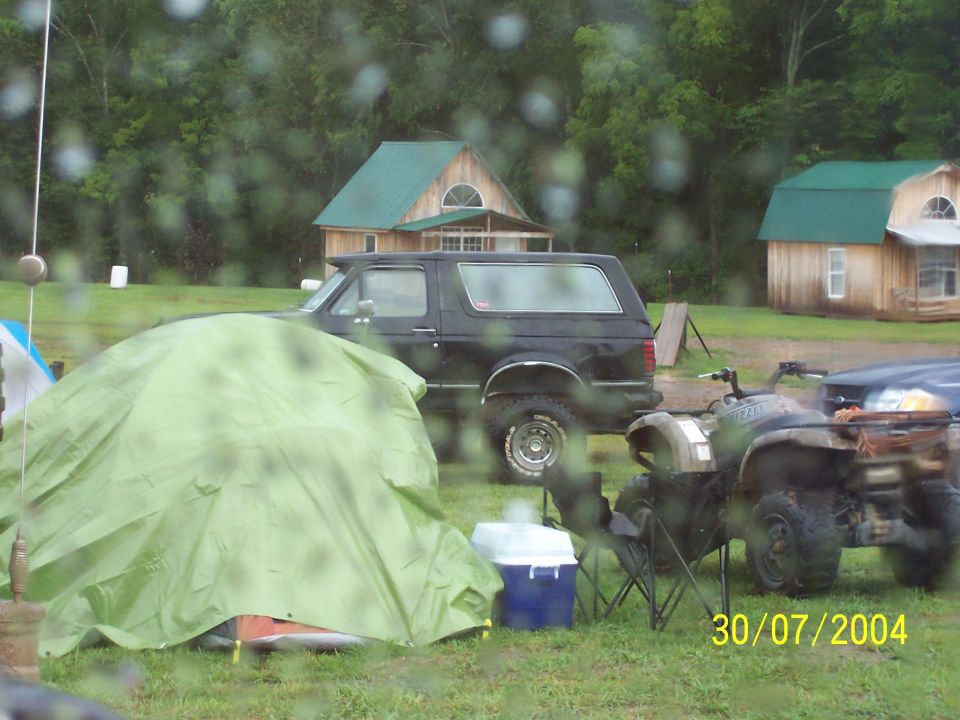 Black SUV parked on grass, side view, with a green tent and ATVs in the foreground